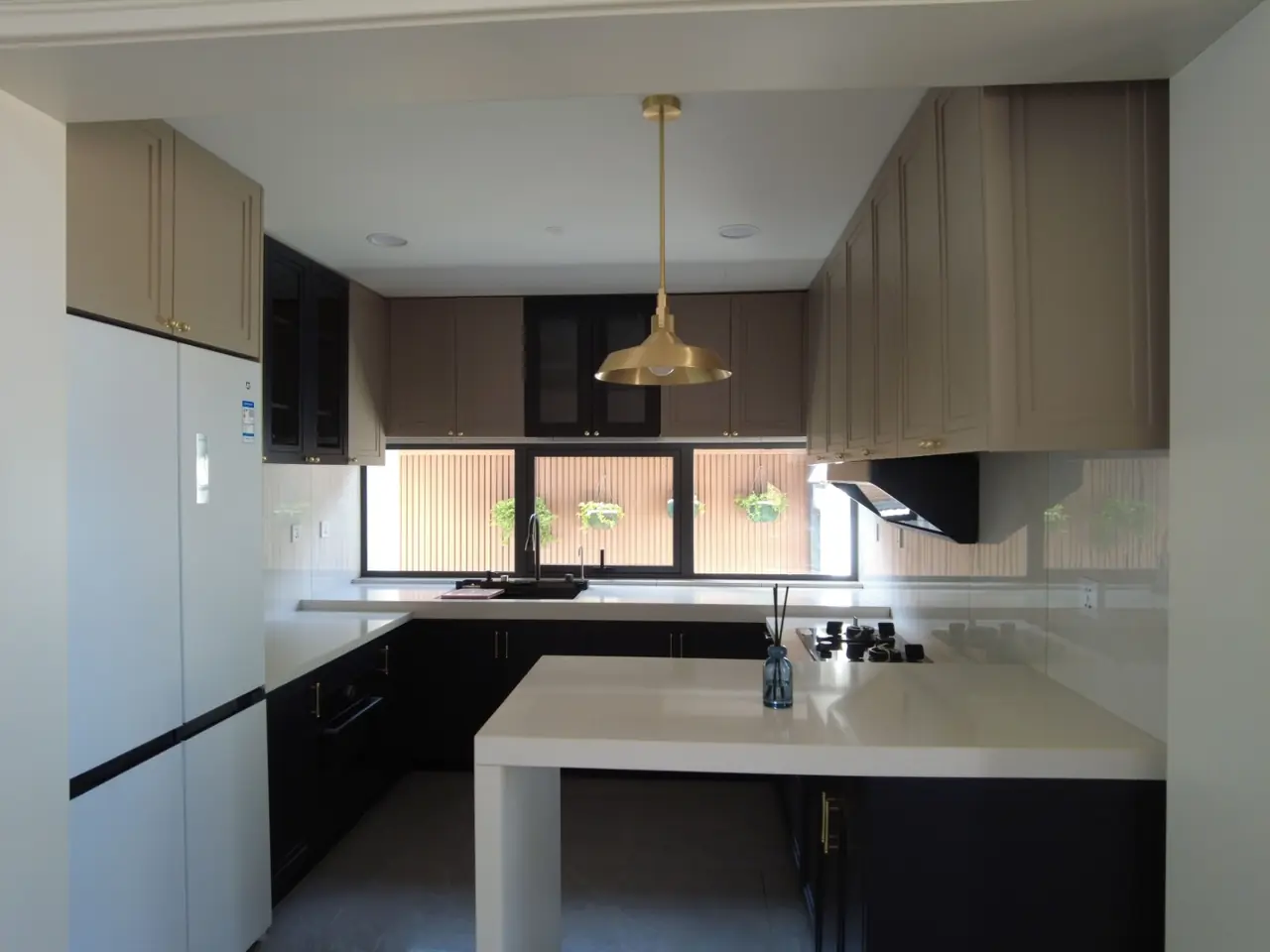 U-shaped fitted kitchen with taupe upper cabinets, navy base units, white worktops, a breakfast peninsula and a brass pendant light